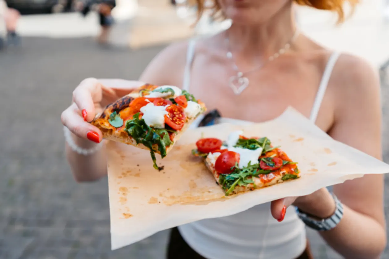 Woman eating slice of gluten-free pizza on streets of Rome